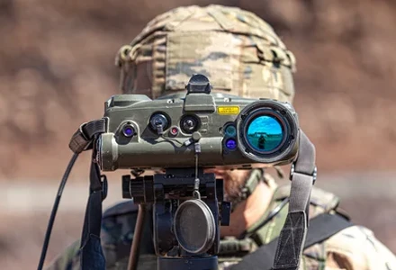 Soldier operating a tripod-mounted laser rangefinder in the field.