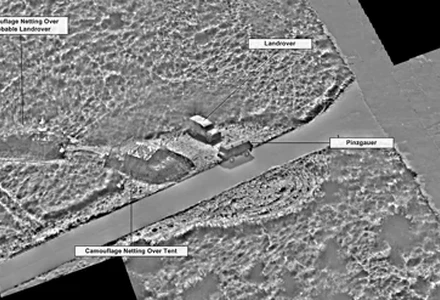 Infrared aerial image highlighting camouflaged vehicles and tent near a road.