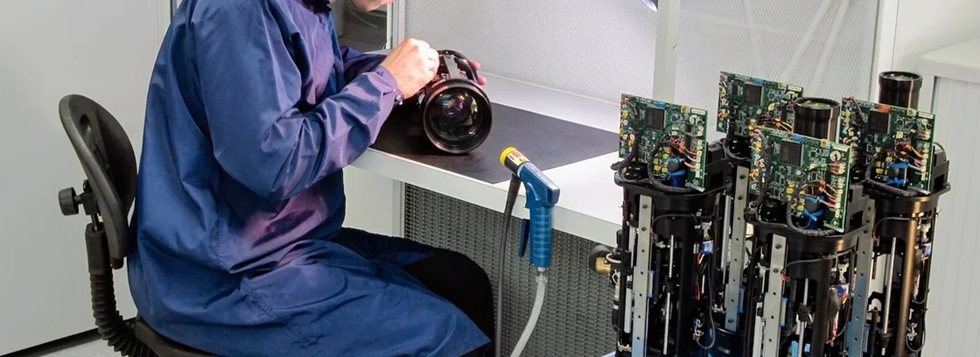 Technician assembling a precision opto‑mechanical system in a cleanroom with multiple production units nearby.